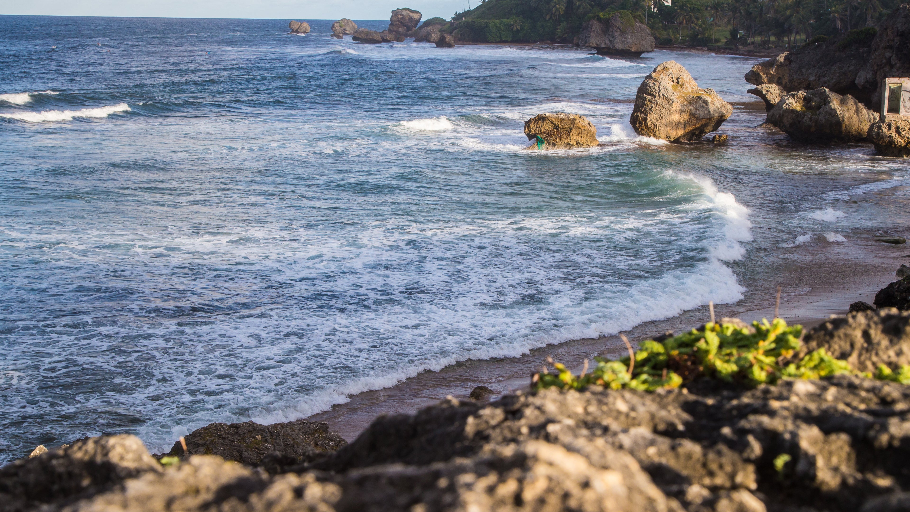 Coastal scene with rocky shoreline and ocean waves, under a partly cloudy sky.